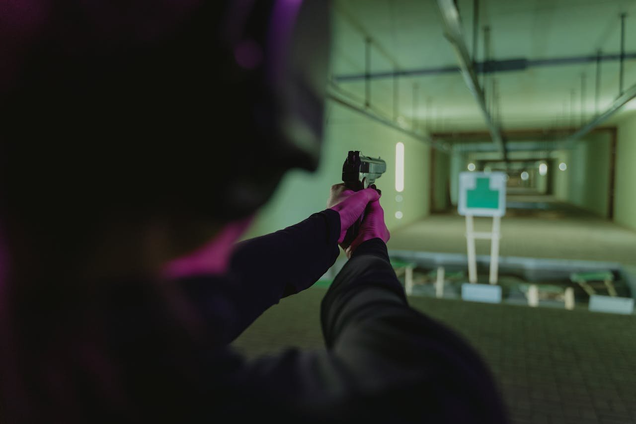 An individual targets a silhouette at an indoor shooting range using a handgun.